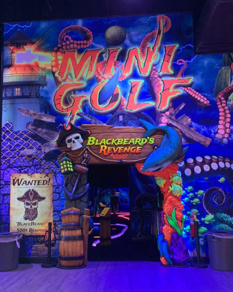 Inside The Rush Funplex, a dark room with neon lights surrounds a lively indoor golf course.
